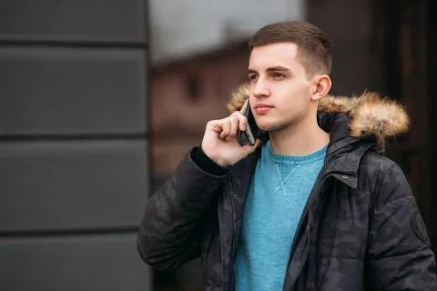 Man in a gray jacket is standing outside and using a phone. Winter Фото