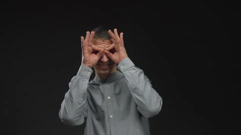 Man in gray shirt making binocular gesture with hands against black isolate.. Stock Footage 314244346