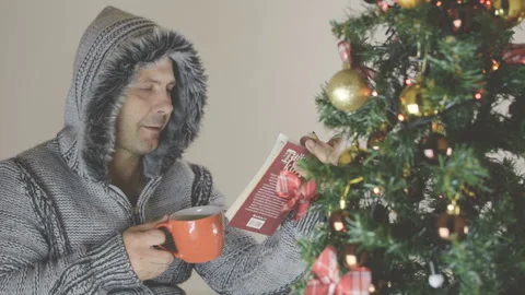 A man in a gray sweater drinks a hot drink. He enthusiastically reads the book. Vídeo Stock 94853433