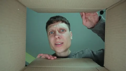 A man in a gray sweater opens a cardboard box, looks inside with a surprised and Stock Footage 303209640
