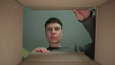 A man in a gray sweater opens a cardboard box, looking inside with a focused Stock Footage 305936030