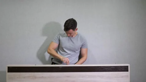 Man in a gray T-shirt assembles furniture using a screwdriver Stock Footage 166616468