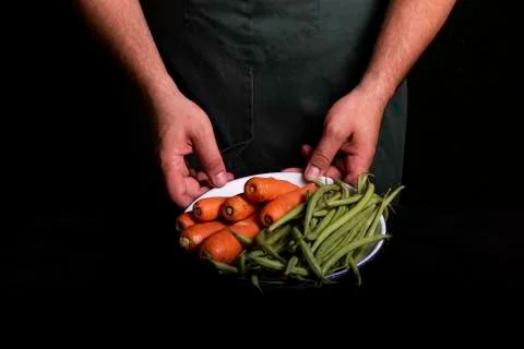 Man with green apron presenting vegetables and garden vegetables. Stock Photos