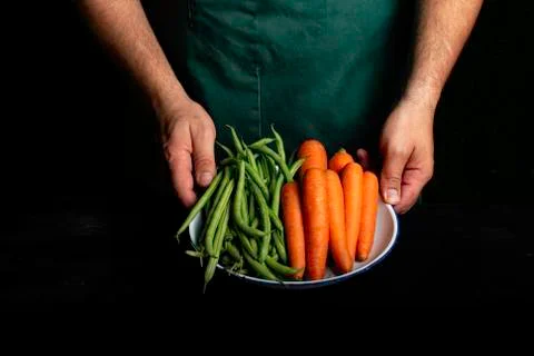Man with green apron presenting vegetables and garden vegetables. Stock Photos