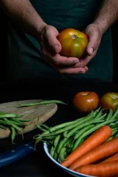 Man with green apron presenting vegetables and garden vegetables. Stock Photos