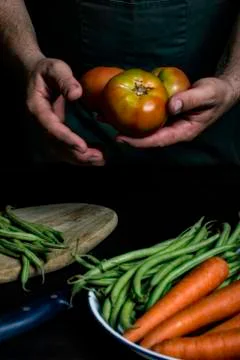 Man with green apron presenting vegetables and garden vegetables. Stock Photos