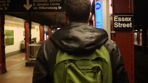 Man with green back pack walks through Essex Street subway station in slow motio Stock Footage 98648516