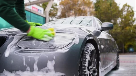 A man in green clothes washes a gray car with foam at a self-service car wash Vidéo 164949682