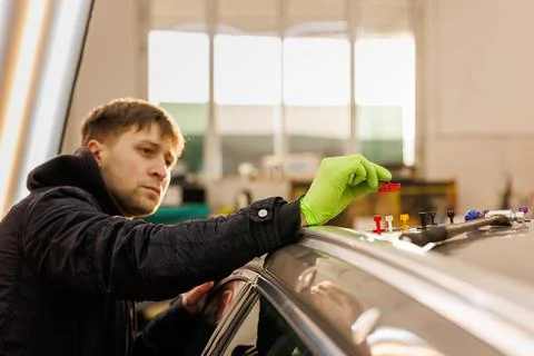 A man in green gloves gestures while working on a car in a garage Stock-Fotos