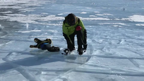 A man in a green jacket and red knee pads puts on skates to skate on ice Video stock 151063237