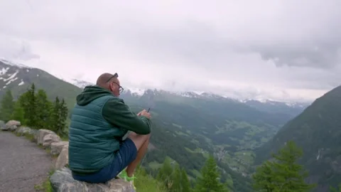 A man in a green jacket sits on a rock, admiring the panoramic view of a Video stock 282230802