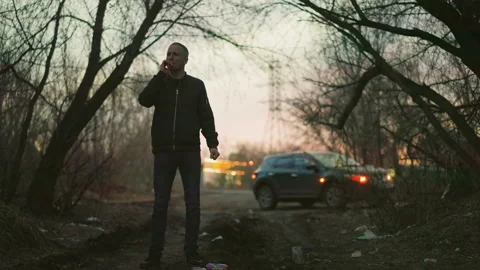 Man in Green Jacket Smoking a Cigarette at Dusk with Car in Background Stock Footage 282297247