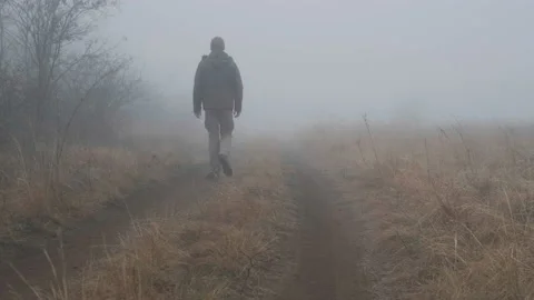 A man in a green jacket is walking on the forest rural  road in thick foggy weat Stock Footage 232400325