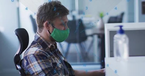 Man with green mask analyzing numeric data on computer monitor at desk with 스톡 사진