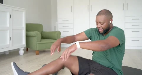 Man in green tee starting workout on home mat doing flutter kicks grabbing green Video stock 337933199
