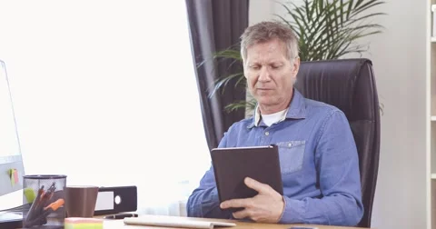 Man with grey hair working with tablet computer at his desk in a home office 스톡 동영상 61135643