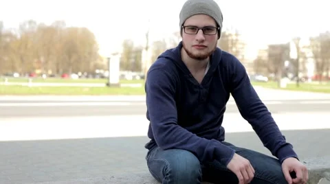 Man in grey hat and glasses sitting near the street and look around (3) Stock-Footage 49535943