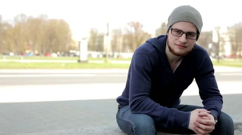 Man in grey hat and glasses sitting near the street and look around (3) Stock Footage 49535954