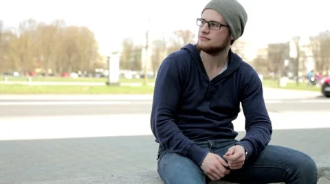 Man in grey hat and glasses sitting near the street and look around (3) Stock-Footage 49536130