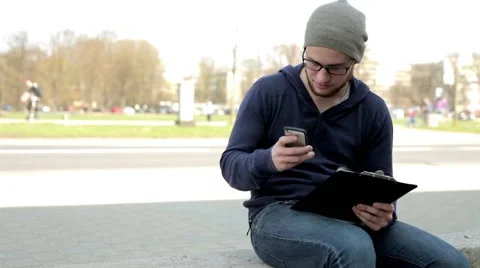 Man in grey hat and glasses sitting near the street and using cellphone. 스톡 동영상 49536285