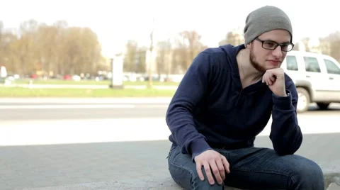 Man in grey hat and glasses sitting near the street and looking on one place Stock Footage 49536354