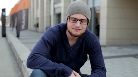 Man in grey hat and glasses sitting near building and looking into camera Stock Footage 49537331