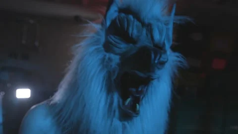 Man in grey wolf mask screams and laughs at camera in darkened room scary Stock Footage 142694960