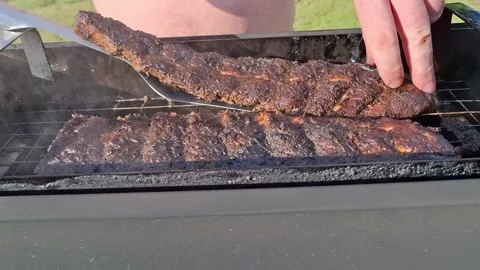 Man grilling BBQ pork ribs on outdoor charcoal grill with tongs smoky barbec Stock Footage 335638094