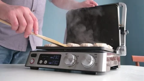 Man grilling meat cutlets on electric home grill Stock Footage 303623792