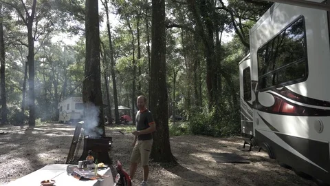 Man Grills Food with Campers and Trees Around Stock Footage