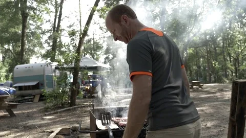 Man Grills Hamburgers with Travel Trailer RV- Stock Footage