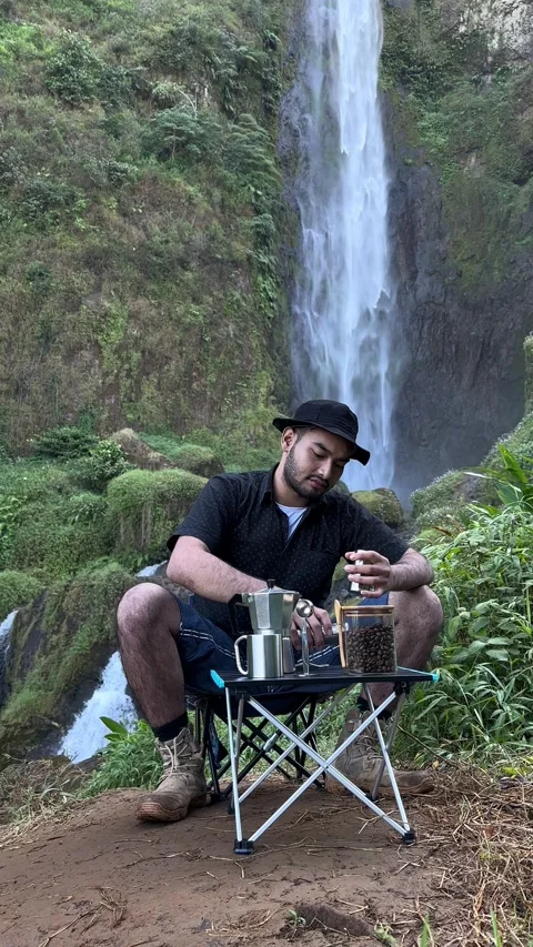 Man Grinding Coffee Beans by Waterfall, Lush Green Nature, Vertical Shot Stock Footage 323907247