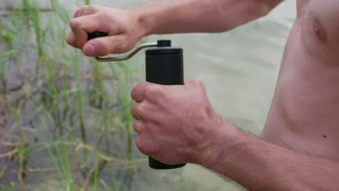 Man Grinding Fresh Coffee Beans with Portable Manual Grinder at Lake Stock Footage 341995179