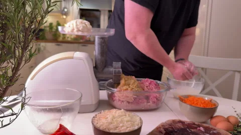 A man is grinding mincemeat through an electric meat grinder in the kitchen, for Stockbeeldmateriaal 304792573