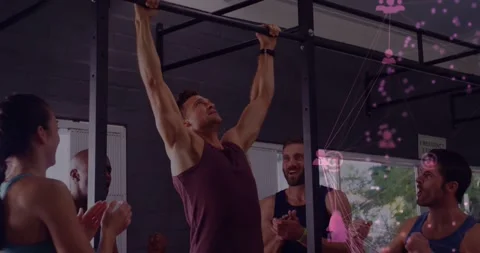 Man gripping bar and pulling up in gym, peers clapping while pink icons Stock Footage 329786403
