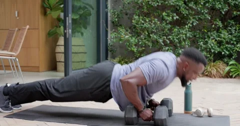 Man gripping dumbbells doing pushups on mat shifting into pike and kneeling, Stock Footage 335366091