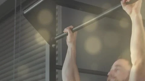 Man gripping pullup bar, performing pullups for strength in gym, warm bokeh Stock Footage 323455694