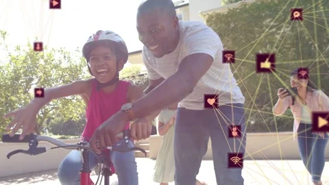Man guiding girl learning on red bike, easing grip while tech icons overlaying, Stock Footage 333936672