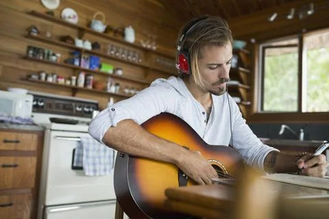 Man with guitar and headphones songwriting cabin table Stock Photos