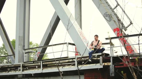A man with a guitar sitting on bridge Stock Footage 50296105