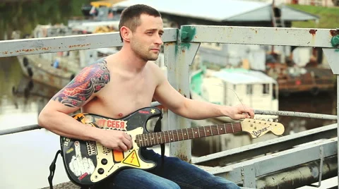 A man with a guitar sitting on bridge Stock Footage 50296633