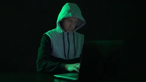 Man is a guy, a hacker in the hood, at the computer, looks at the monitor and Stock Footage 122065859