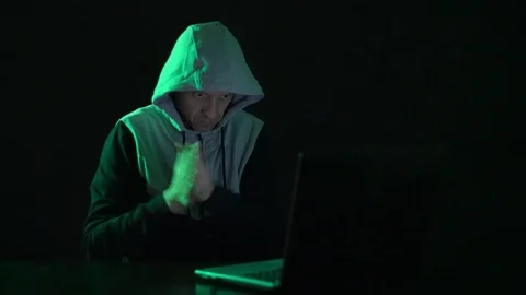 Man is a guy, a hacker in the hood, at the computer, looks at the monitor and Stock Footage 122085531
