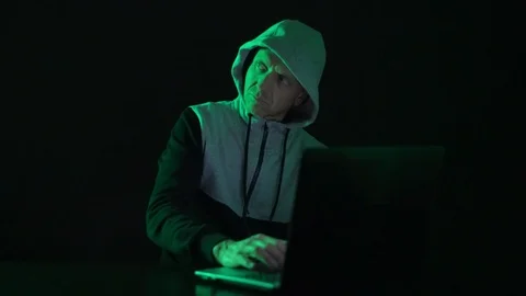 Man is a guy, a hacker in the hood, at the computer, looks at the monitor and Stock Footage 122085545