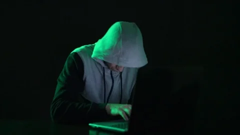 Man is a guy, a hacker in the hood, at the computer, looks at the monitor and Stock Footage 122098383