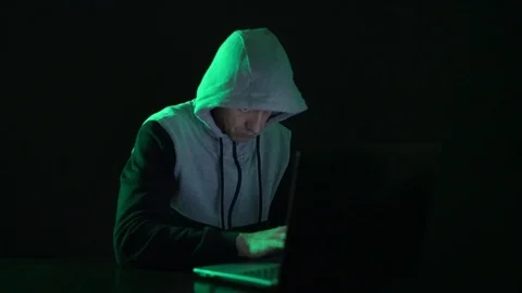 Man is a guy, a hacker in the hood, at the computer, looks at the monitor and Stock Footage 122098393