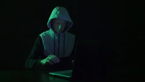Man is a guy, a hacker in the hood, at the computer, looks at the monitor and Stock Footage 123169734