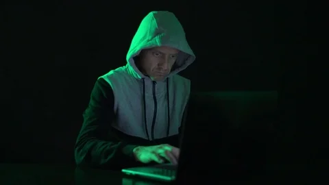 Man is a guy, a hacker in the hood, at the computer, looks at the monitor and Stock Footage 123702869