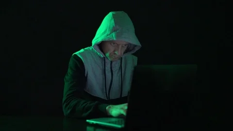 Man is a guy, a hacker in the hood, at the computer, looks at the monitor and Stock Footage 124341409