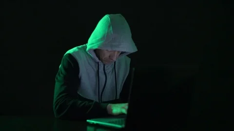 Man is a guy, a hacker in the hood, at the computer, looks at the monitor and Stock Footage 124619317